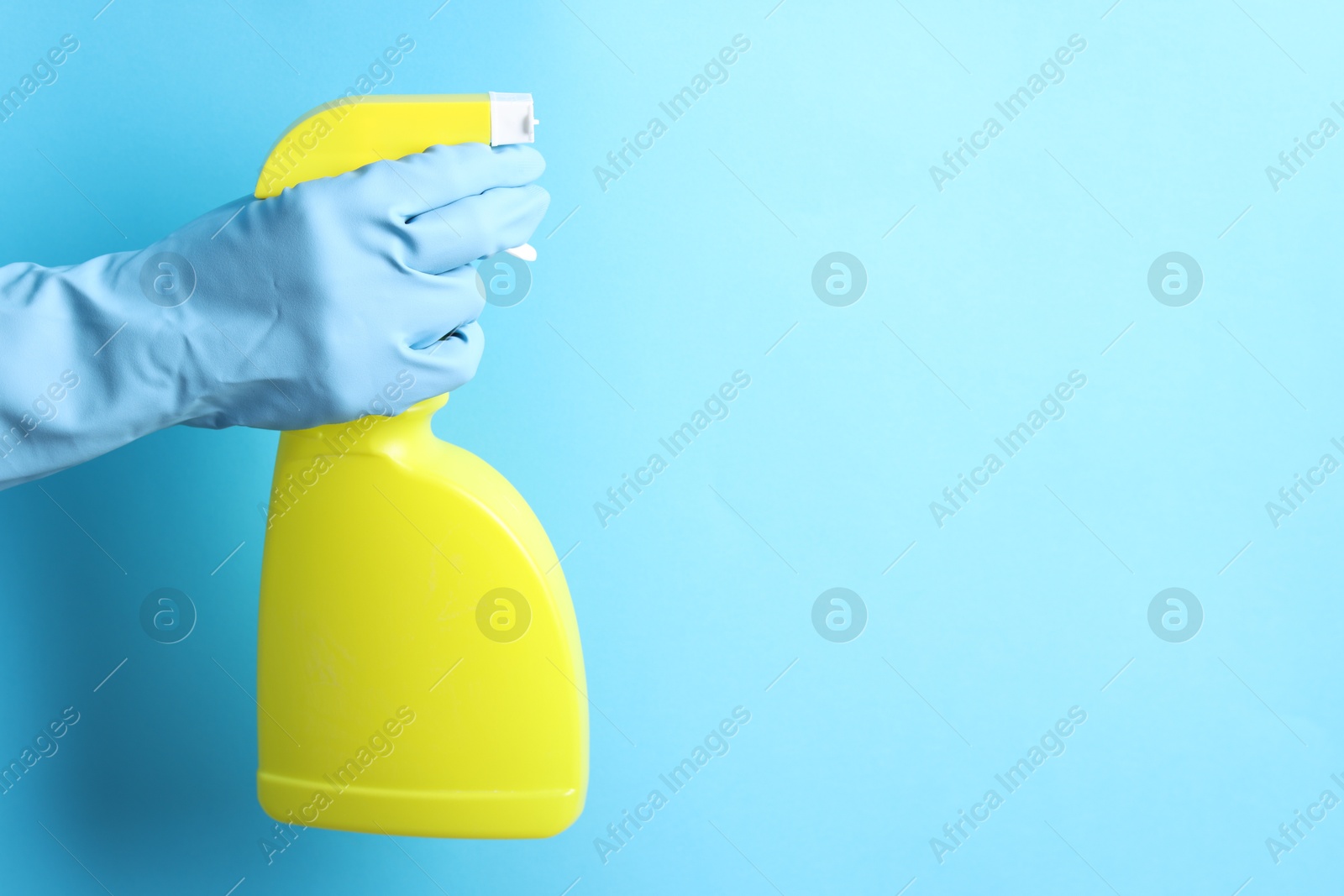 Photo of Woman with spray bottle of cleaning product on light blue background, closeup. Space for text