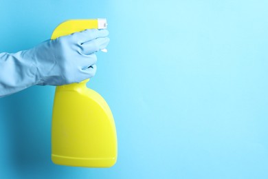 Photo of Woman with spray bottle of cleaning product on light blue background, closeup. Space for text