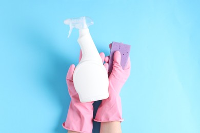 Photo of Woman with spray bottle of cleaning product and sponge on light blue background, top view