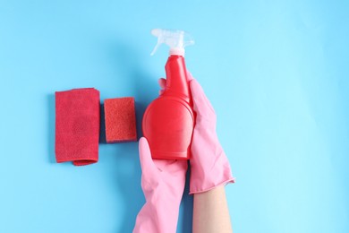 Photo of Woman with spray bottle of cleaning product, rag and sponge on light blue background, top view