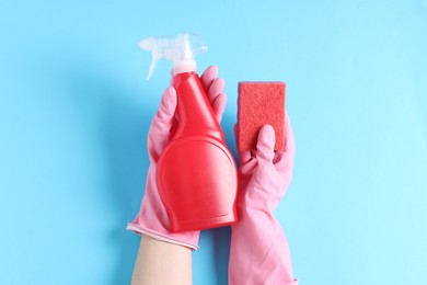 Photo of Woman with spray bottle of cleaning product and sponge on light blue background, top view