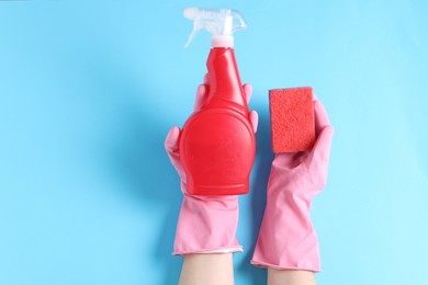 Photo of Woman with spray bottle of cleaning product and sponge on light blue background, top view. Space for text