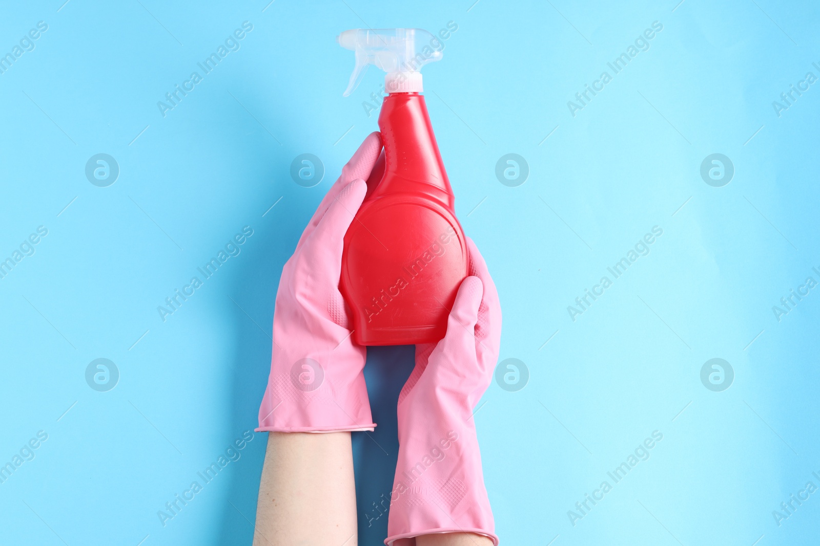 Photo of Woman with spray bottle of cleaning product on light blue background, top view