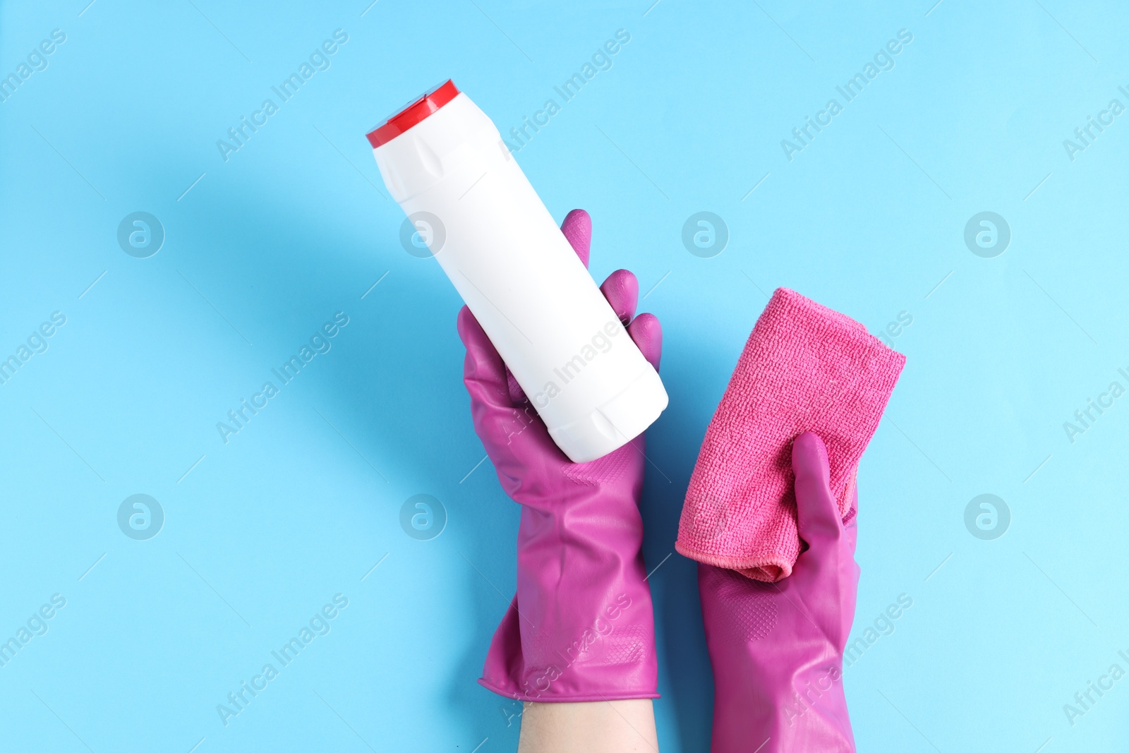 Photo of Woman with bottle of cleaning product and rag on light blue background, top view. Space for text