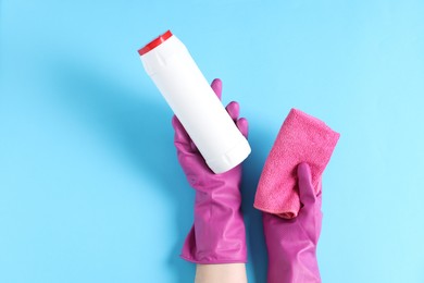 Photo of Woman with bottle of cleaning product and rag on light blue background, top view. Space for text