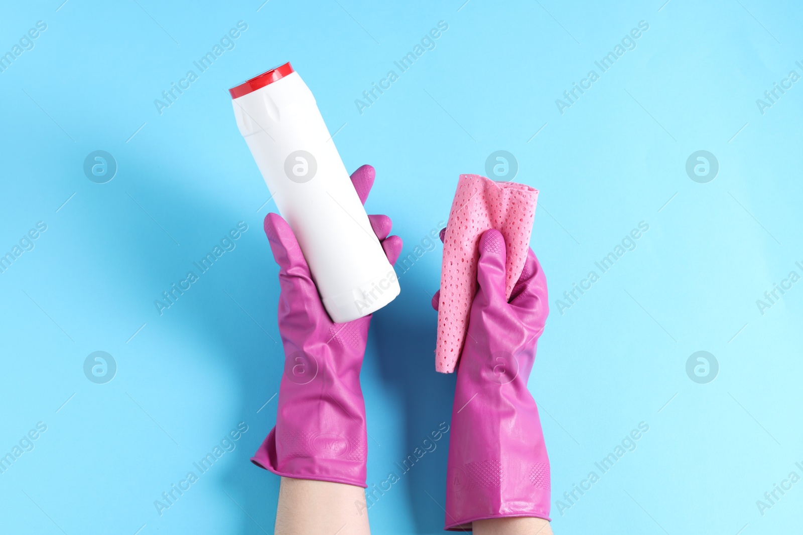 Photo of Woman with bottle of cleaning product and rag on light blue background, top view