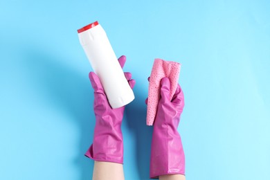 Photo of Woman with bottle of cleaning product and rag on light blue background, top view