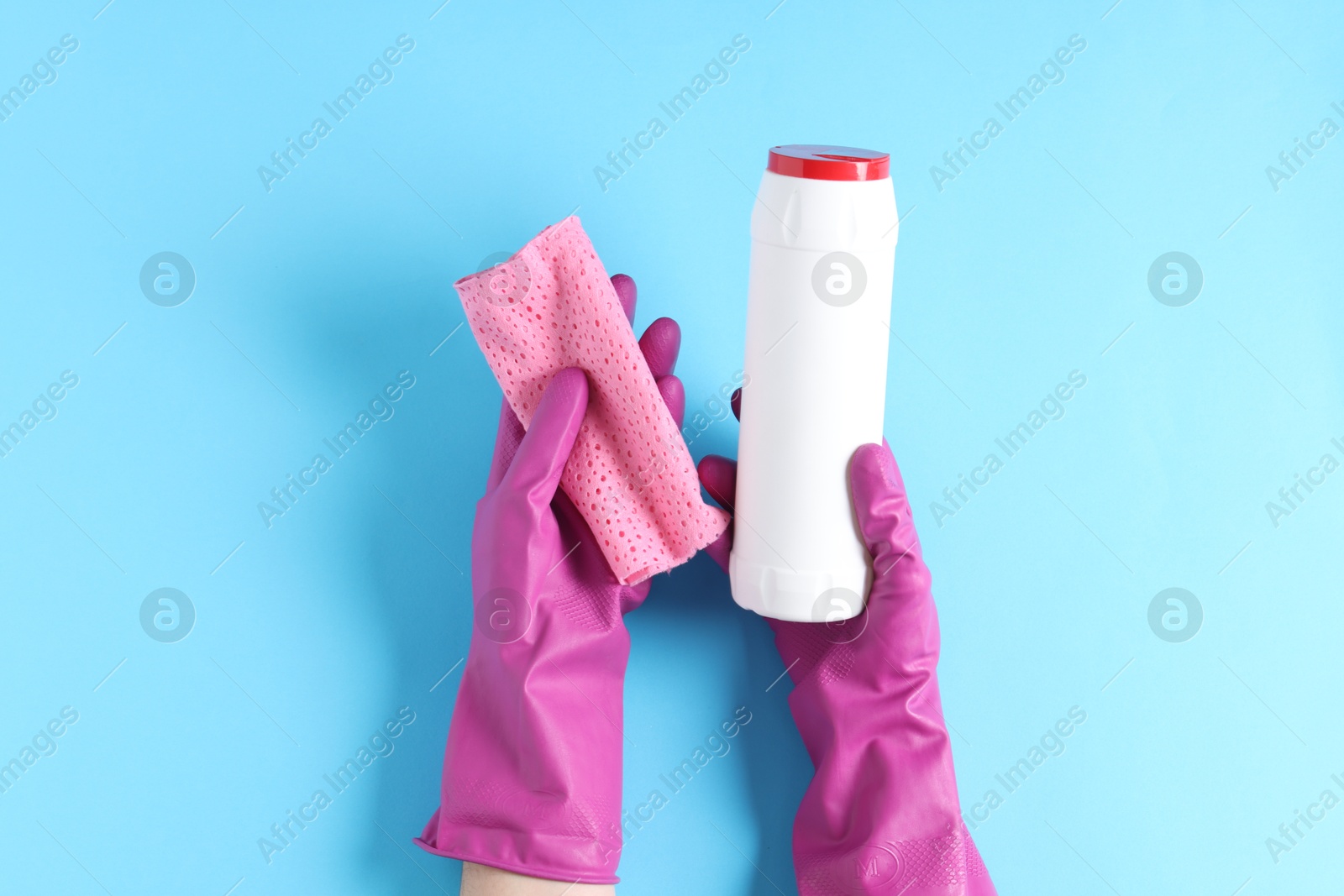 Photo of Woman with bottle of cleaning product and rag on light blue background, top view