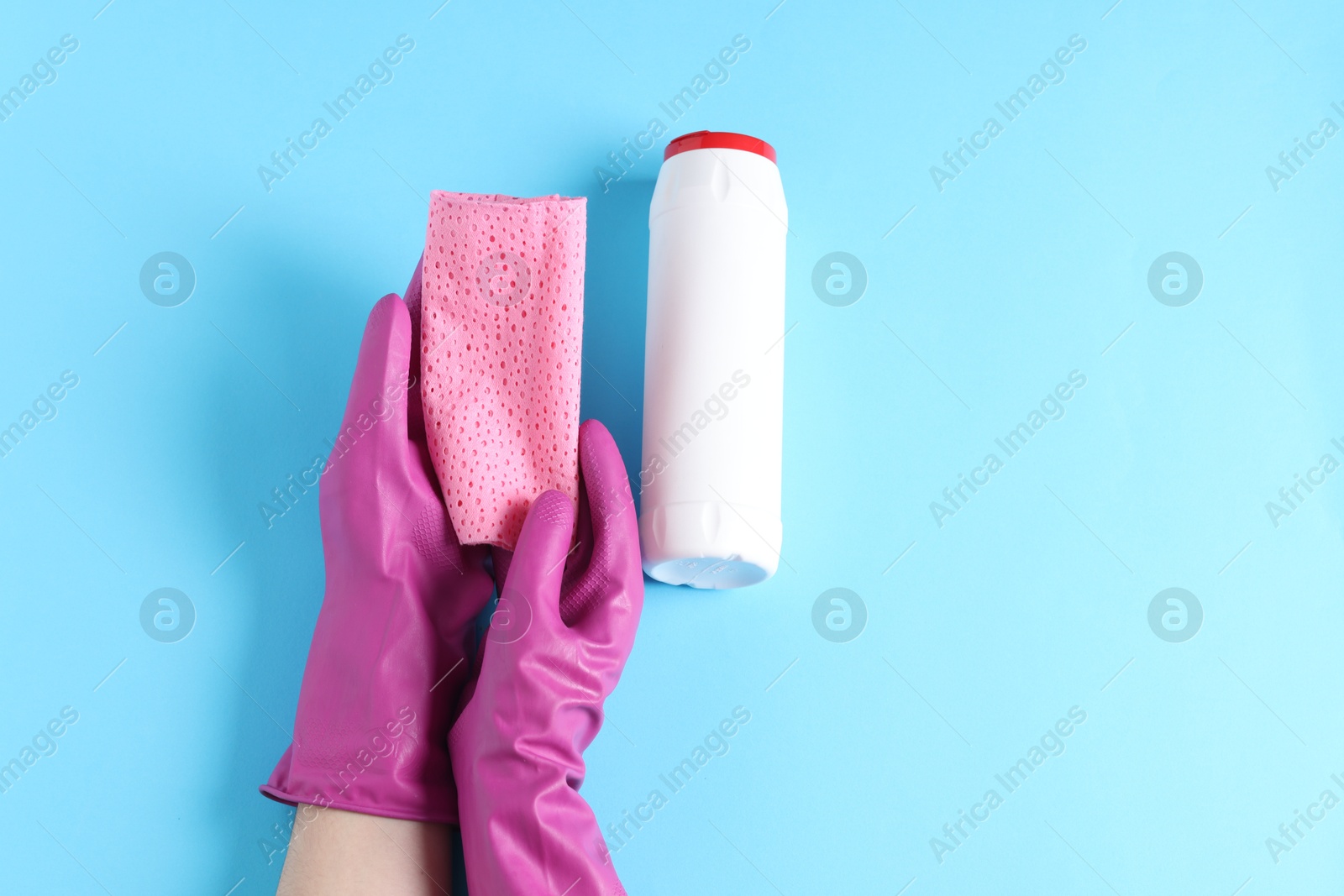 Photo of Woman with rag and bottle of cleaning product on light blue background, top view. Space for text