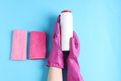 Photo of Woman with bottle of cleaning product and rags on light blue background, top view