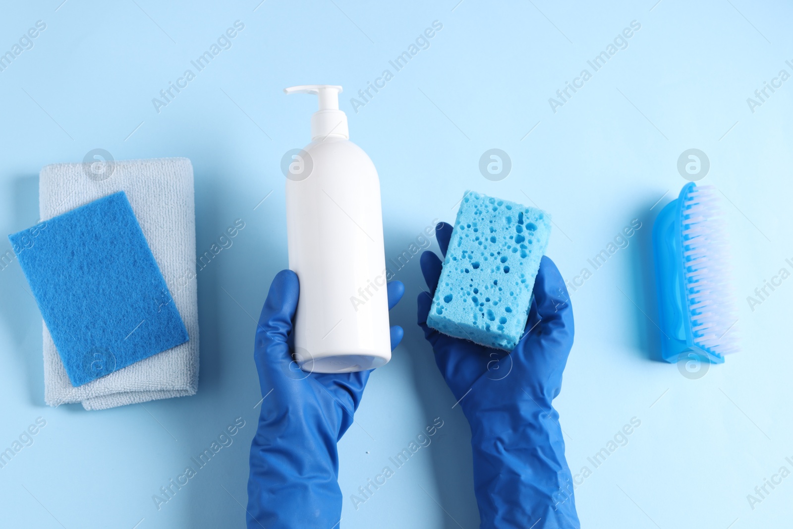 Photo of Woman with bottle of cleaning product and supplies on light blue background, top view