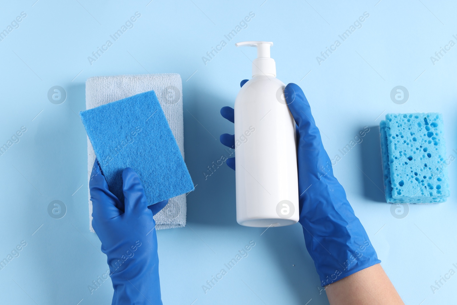 Photo of Woman with bottle of cleaning product and supplies on light blue background, top view