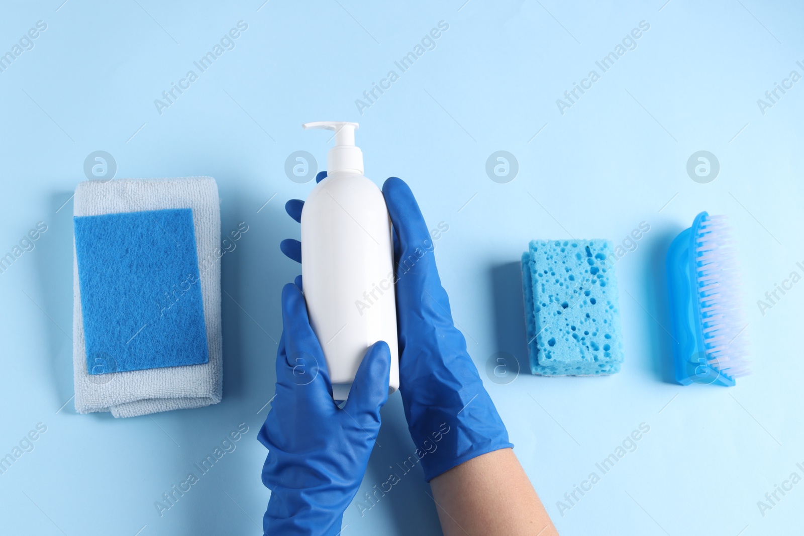 Photo of Woman with bottle of cleaning product and supplies on light blue background, top view