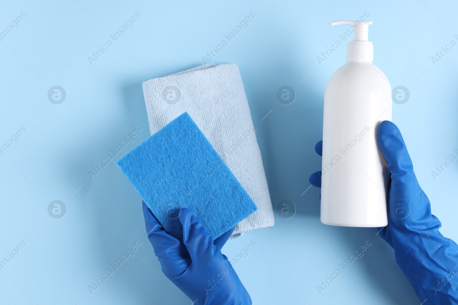 Photo of Woman with bottle of cleaning product and supplies on light blue background, top view. Space for text