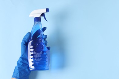 Photo of Woman with spray bottle of cleaning product on light blue background, top view. Space for text