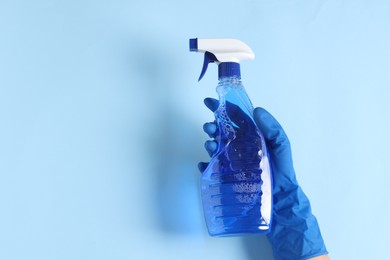 Photo of Woman with spray bottle of cleaning product on light blue background, top view. Space for text