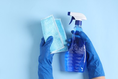 Photo of Woman with spray bottle of cleaning product and rag on light blue background, top view. Space for text