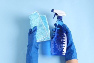 Photo of Woman with spray bottle of cleaning product and rag on light blue background, top view