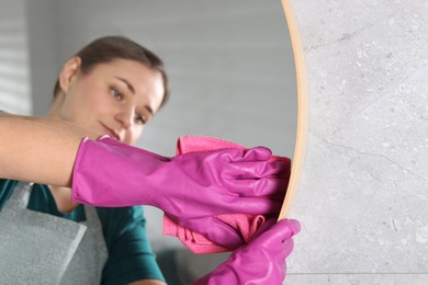 Photo of Woman cleaning mirror with rag indoors, selective focus