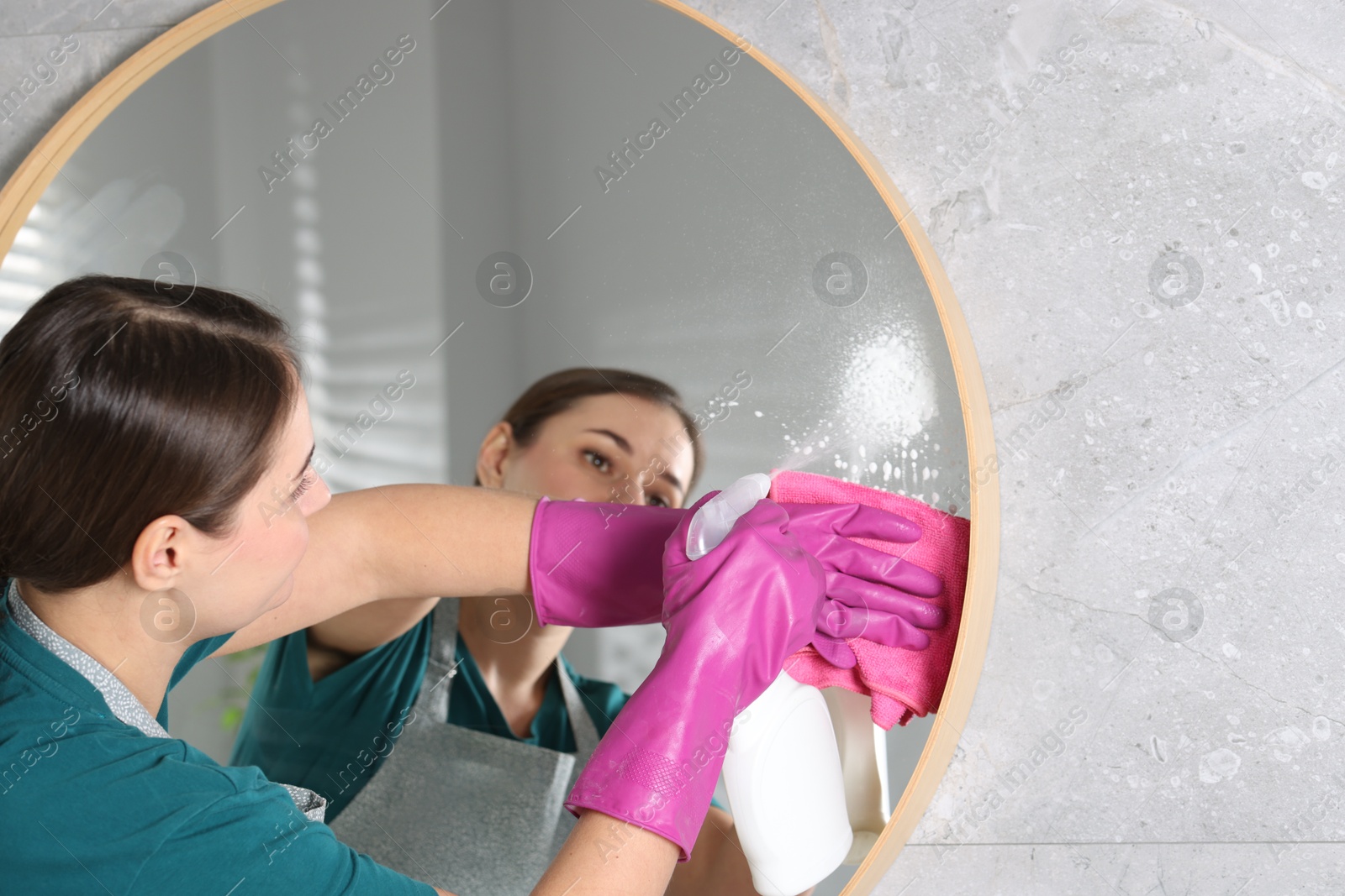 Photo of Woman using cleaning product while wiping mirror with rag indoors, space for text