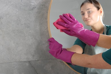 Photo of Woman cleaning mirror with rag indoors, space for text