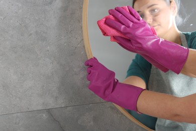 Photo of Woman cleaning mirror with rag indoors, space for text