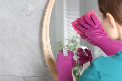 Photo of Woman using cleaning product while wiping mirror with rag indoors, closeup. Space for text