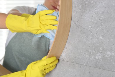 Woman cleaning mirror with rag indoors, closeup. Space for text