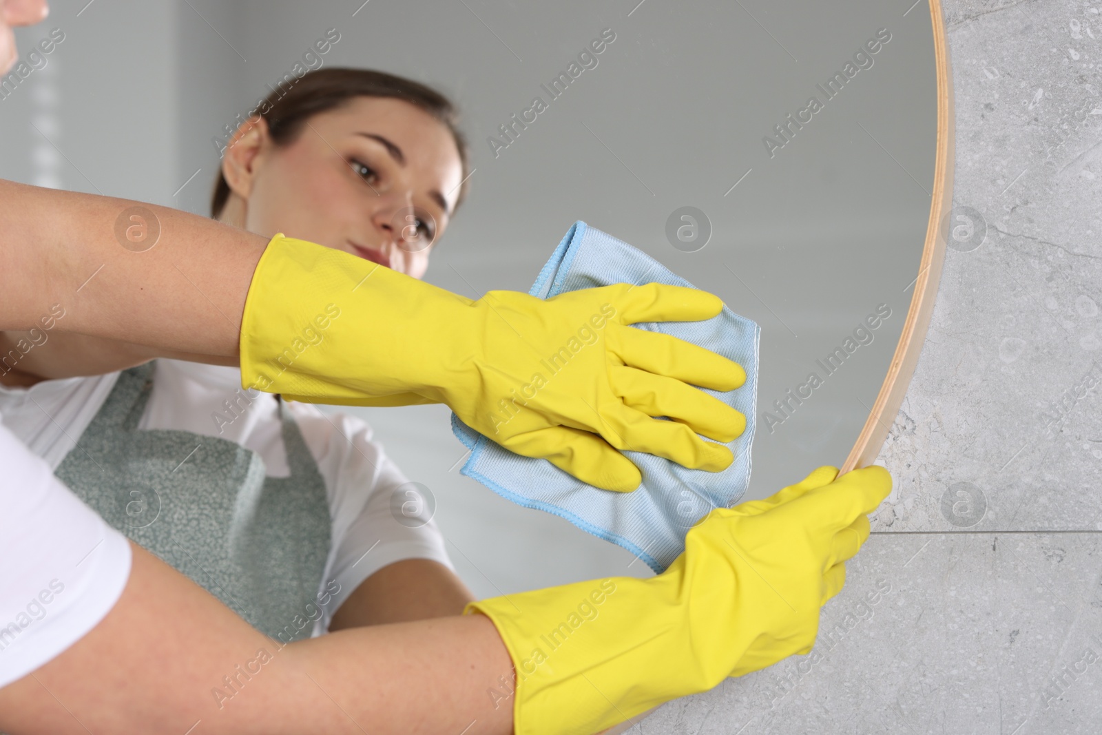 Photo of Woman in gloves cleaning mirror with rag indoors