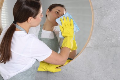 Photo of Woman cleaning mirror with rag indoors, space for text