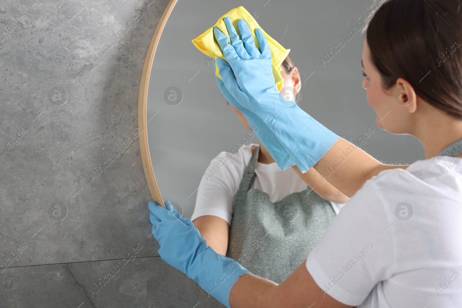 Photo of Woman cleaning mirror with rag indoors, space for text