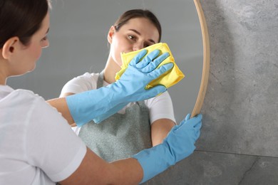 Photo of Woman cleaning mirror with rag indoors, space for text