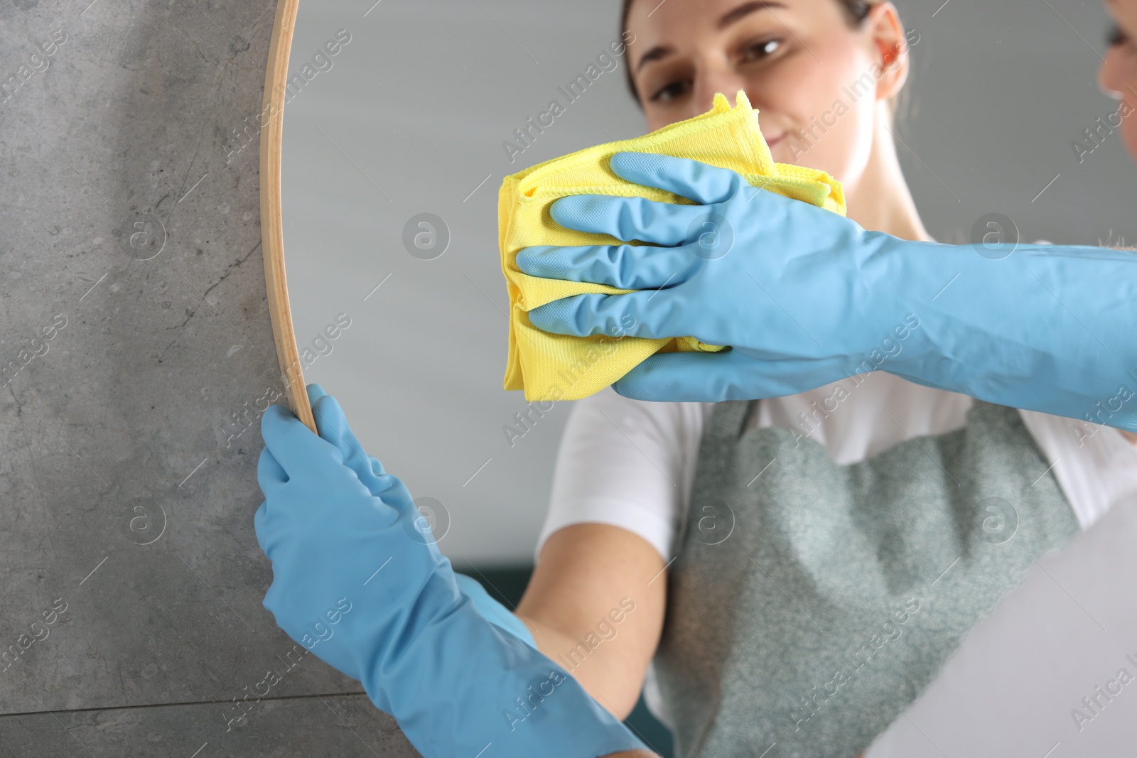 Photo of Woman in gloves cleaning mirror with rag indoors