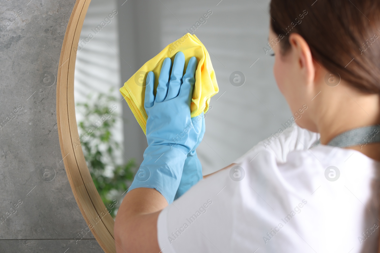 Photo of Woman cleaning mirror with microfiber cloth indoors