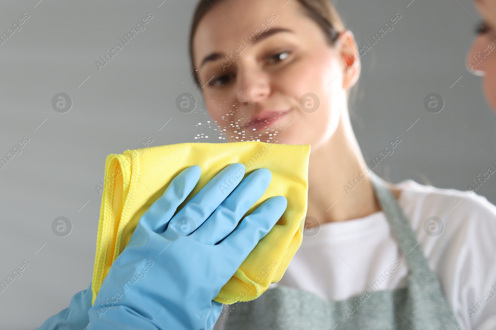 Photo of Woman cleaning mirror with microfiber cloth indoors