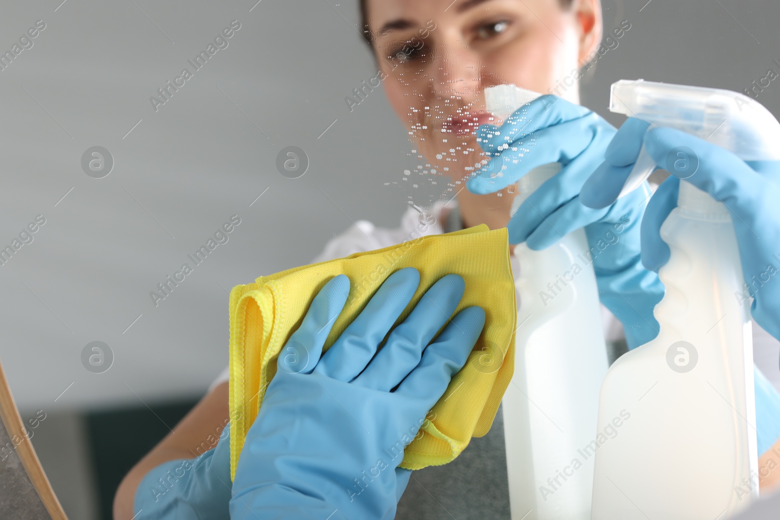 Photo of Woman using cleaning product while wiping mirror with rag indoors, space for text