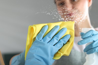 Photo of Woman using cleaning product while wiping mirror with rag indoors, closeup