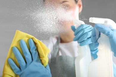 Photo of Woman using cleaning product while wiping mirror with rag indoors