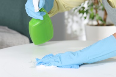 Photo of Woman using cleaning product while wiping table with rag indoors, closeup