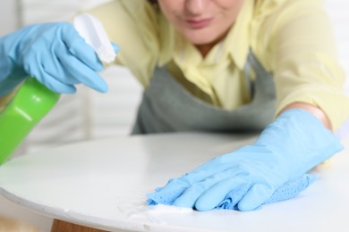 Photo of Woman using cleaning product while wiping table with rag indoors, closeup