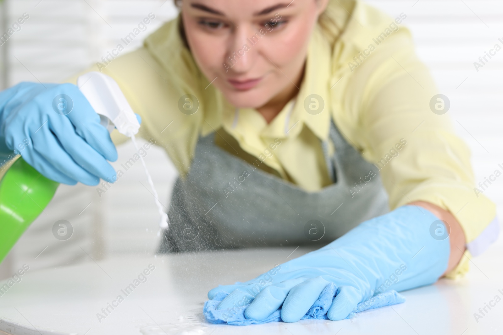 Photo of Woman using cleaning product while wiping table with rag indoors, selective focus