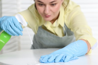 Photo of Woman using cleaning product while wiping table with rag indoors, selective focus