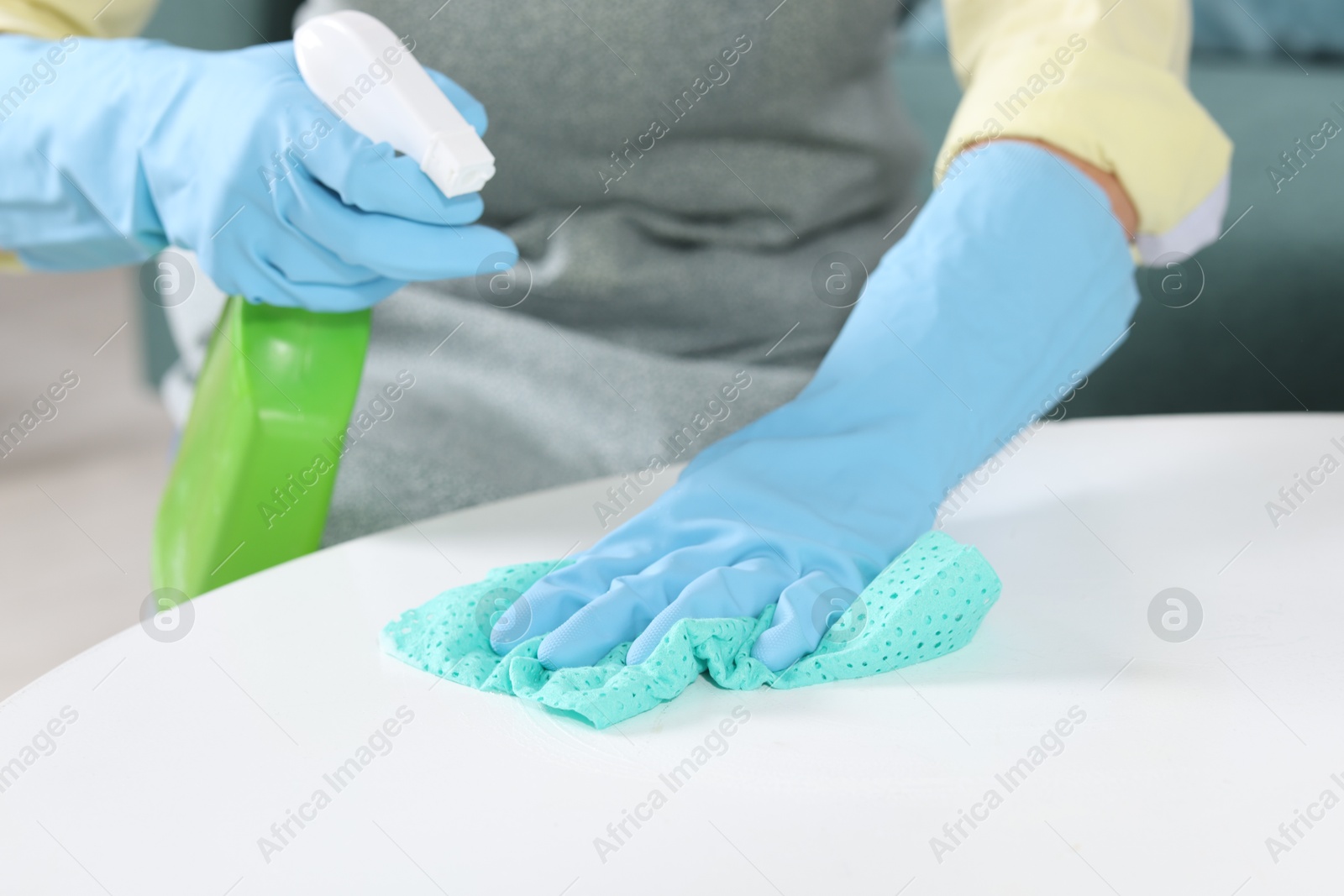 Photo of Woman using cleaning product while wiping table with rag indoors, closeup