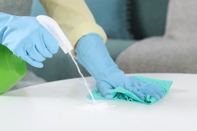 Photo of Woman using cleaning product while wiping table with rag indoors, closeup