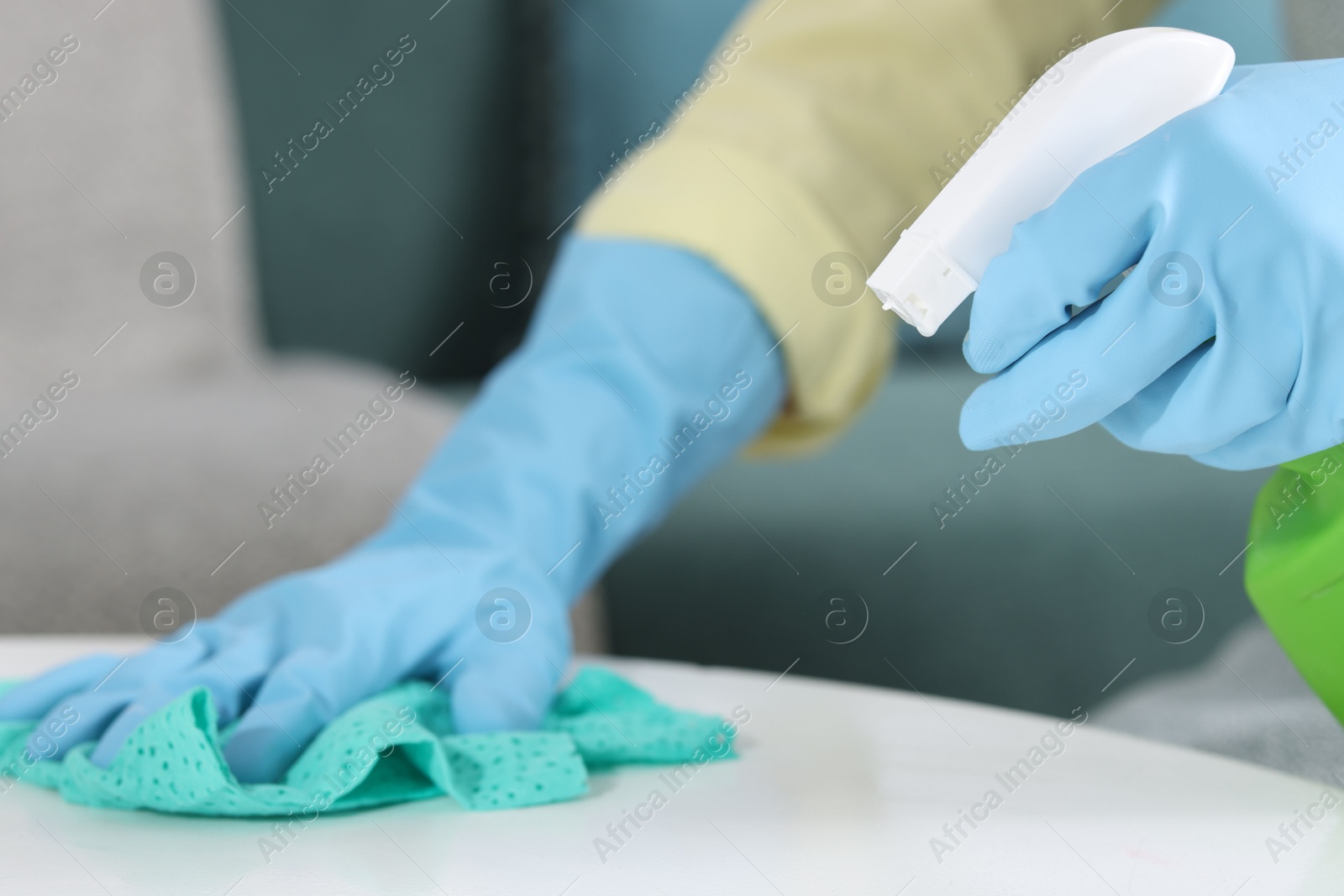 Photo of Woman using cleaning product while wiping table with rag indoors, closeup