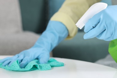 Photo of Woman using cleaning product while wiping table with rag indoors, closeup