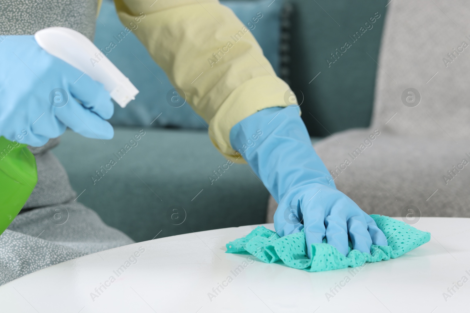 Photo of Woman using cleaning product while wiping table with rag indoors, closeup