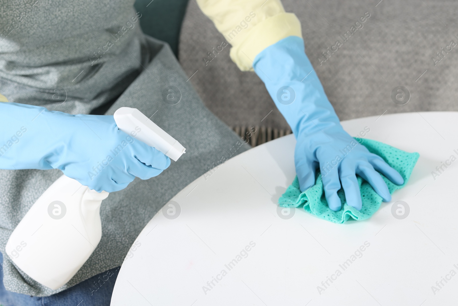 Photo of Woman using cleaning product while wiping table with rag indoors, closeup