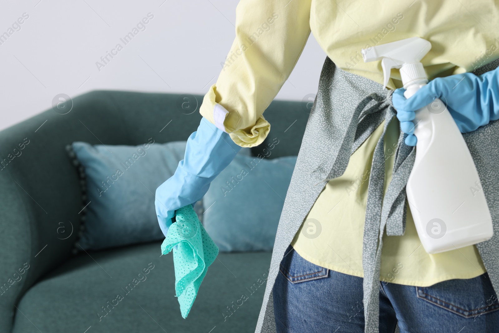 Photo of Woman with rag hiding spray bottle of cleaning product behind her back indoors, closeup. Space for text