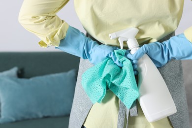 Photo of Woman hiding spray bottle of cleaning product and rag behind her back indoors, closeup. Space for text